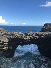 Distant view of woman walking on rock over sea against sky