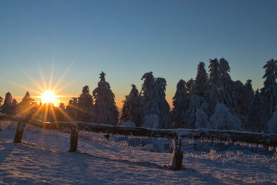 Snow covered field against sky during sunset