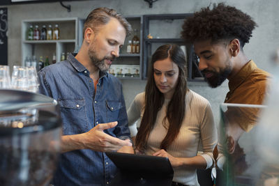 Cafe owner sharing tablet pc with baristas in coffee shop