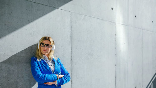 Panoramic view of businesswoman listening music on headphones while standing outdoors