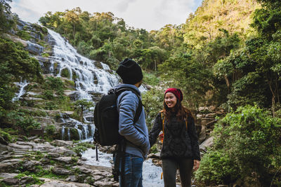 Smiling woman with friend standing by waterfall in forest
