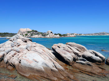 Scenic view of rocks by sea against clear blue sky