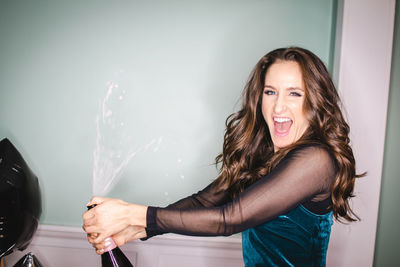 Portrait of woman spraying champagne against wall