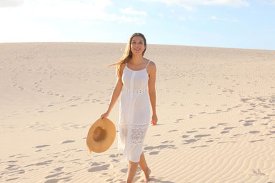 Portrait of smiling young woman walking on sand at desert