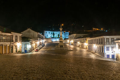 Illuminated street amidst buildings in city at night