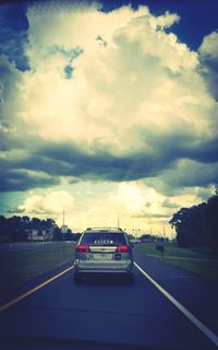 Cars on road against cloudy sky