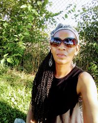 Portrait of young woman wearing sunglasses standing against plants