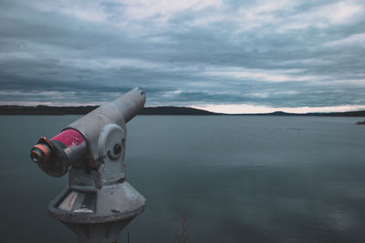 Close-up of coin-operated binoculars on sea against sky