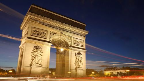 Light trails by arc de triomphe in city at night