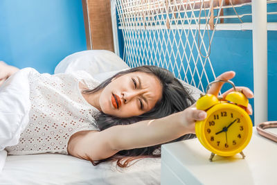 Young woman holding alarm clock while sleeping on bed