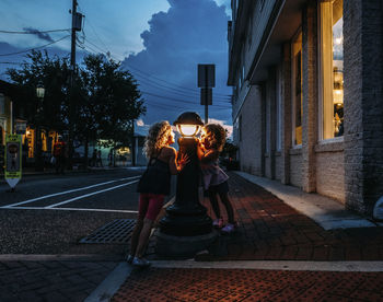 Sisters looking at lamp post while standing at sidewalk in city