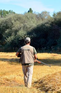 Rear view of man holding rifle while walking on land