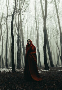 Woman standing by tree trunk in forest