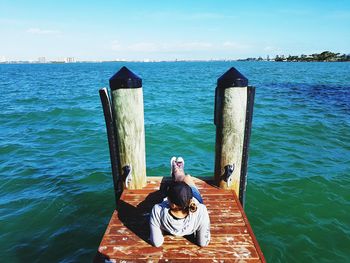 Woman sitting by sea against sky