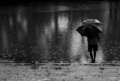 Rear view of man with umbrella fishing in lake