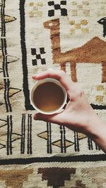 Cropped hand holding coffee cup over carpet at home