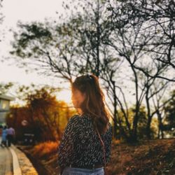 Side view of woman standing against trees during sunset