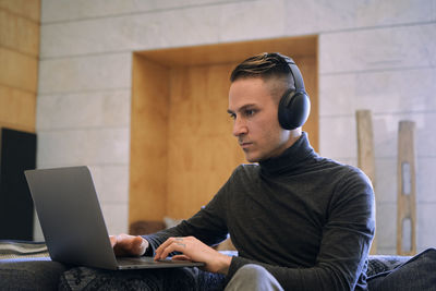 Young businessman in headphones having video call via netbook at hotel lobby