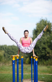 Portrait of young woman stretching on parallel bars in park