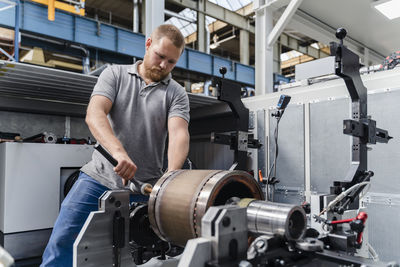 Young industry laborer tightening bolts of machine while standing at factory