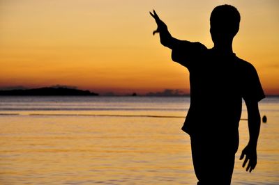 Rear view of silhouette man gesturing at beach during sunset