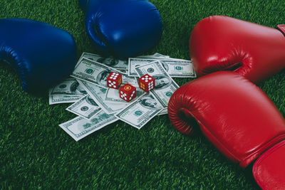 High angle view of red and blue boxing gloves with paper currency and dice on carpet