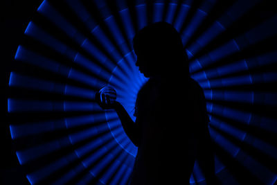 Silhouette girl holding crystal ball while standing against illuminated blue lights