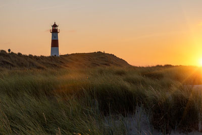 Lighthouse on field against sky during sunset