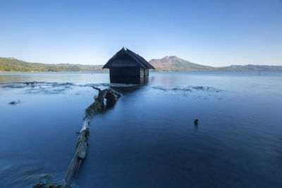 House by lake against clear blue sky