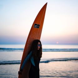 Woman wearing sunglasses on beach against sky during sunset