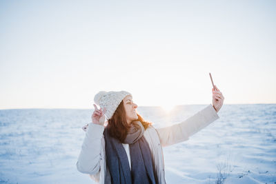 Smiling woman doing selfie while standing on snow covered land during winter