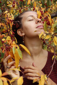 Close-up of young woman with flowers in autumn leaves