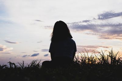 Rear view of woman looking at field against sky during sunset