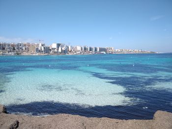 Scenic view of sea and buildings against clear blue sky