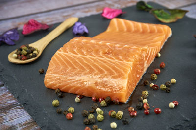 Fresh salmon fillets on black cutting board with herbs and spice