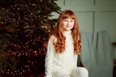 Happy young girl sitting by the christmas tree
