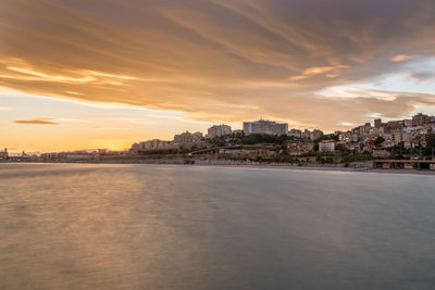 Sea by buildings against sky during sunset