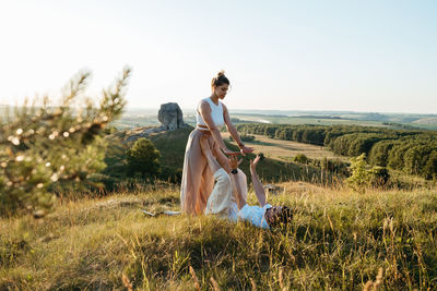 Man and woman practicing yoga outdoors at sunset with scenic landscape