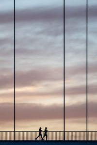 Silhouette people walking on bridge against sky during sunset