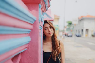 Portrait of young woman standing by wall in city