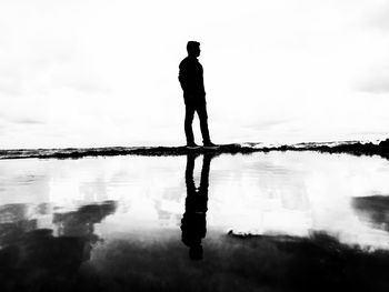 Rear view of silhouette man standing by sea against sky