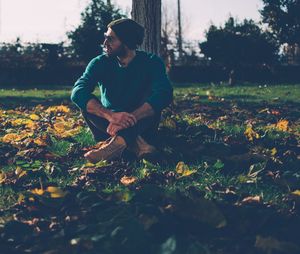 Man looking away while sitting against tree trunk on field