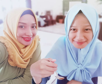 Portrait of smiling sisters wearing hijab at home