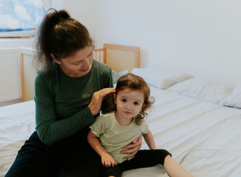 A young girl with a child with a cast on her leg are sitting on the bed.