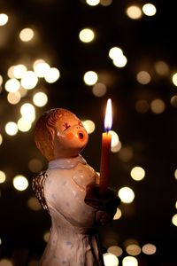 Statue of angel holding lit candle against defocussed lights