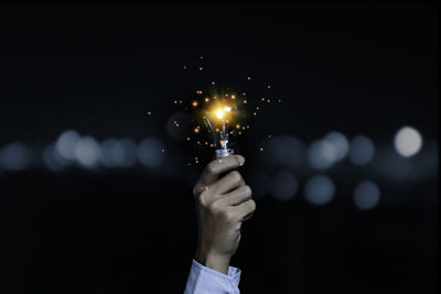 Cropped hand holding illuminated light bulb at night