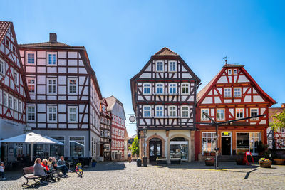 People on street by buildings against blue sky