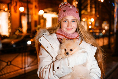 Cute girl holds spitz in her arms in evening on street in light of street