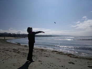 Full length of boy throwing pebble in sea against sky