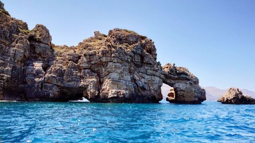 Rock formation in sea against clear blue sky